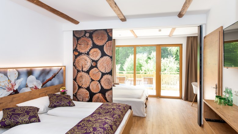 Ein modernes Familienzimmer mit Holzboden, zwei Betten, gro&szlig;en Fenstern und dekorativen Holzelementen.