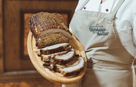 Gefüllte Schweinebrust auf Holzplatte, serviert von Person in Schürze.