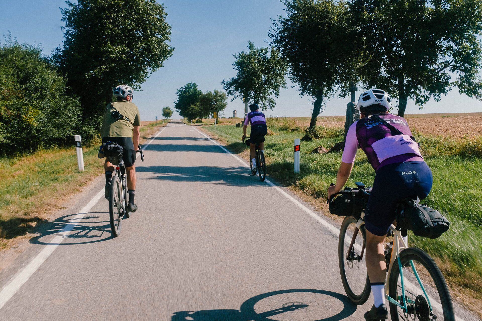 Drei Radfahrer genießen die sanfte Brise und die malerische Landschaft entlang des Iron Curtain Trails. Umgeben von üppigem Grün und dem strahlend blauen Himmel, vermittelt die Szenerie ein Gefühl von Freiheit und Abenteuer. Die ruhige Straße lädt dazu ein, die Schönheit der Natur in vollen Zügen zu erleben.
