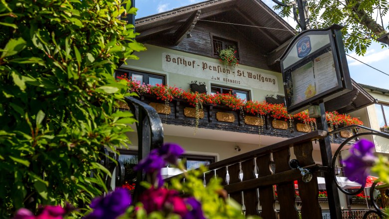 Gasthof Pension St. Wolfgang mit Blumen geschm&uuml;cktem Balkon und Schild im Vordergrund.