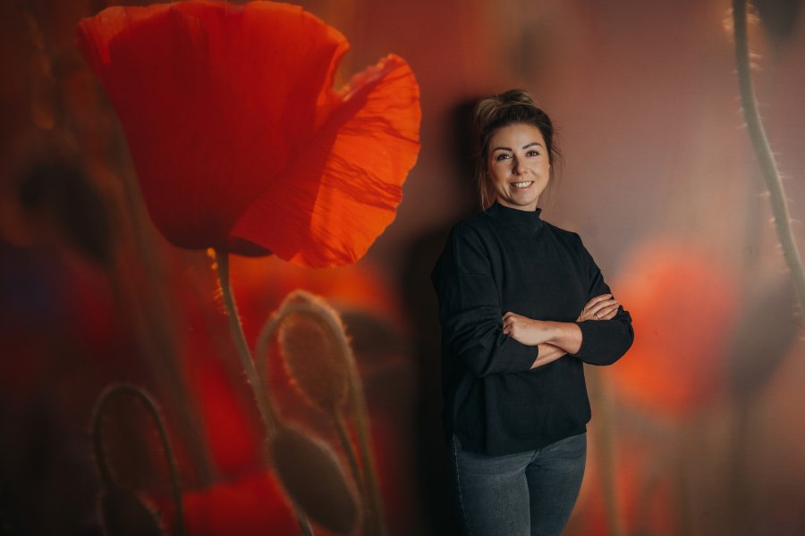 Frau steht vor einer Wand mit Mohnblumenmotiv.