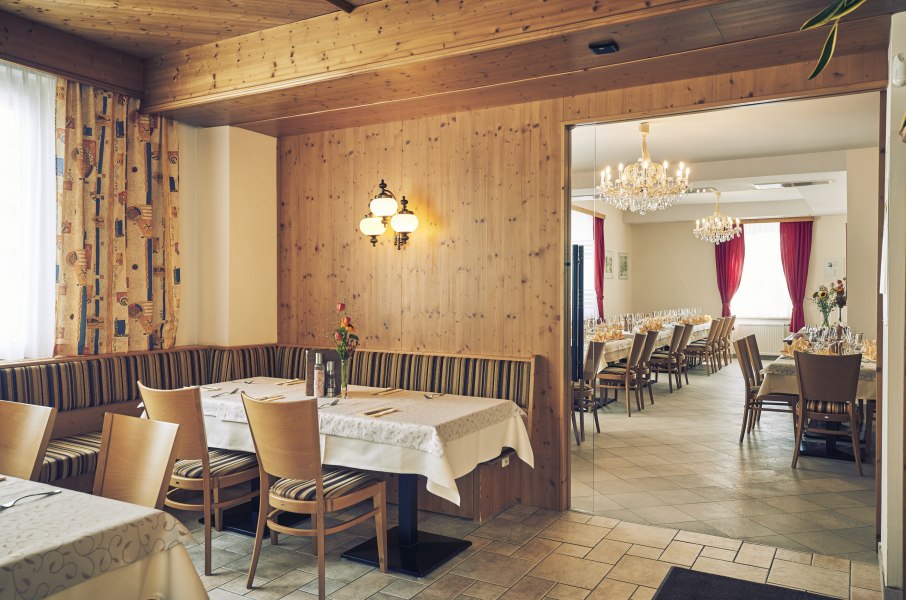 Ein gemütliches Gastzimmer mit Holzwänden und ein angrenzender Festsaal mit Kronleuchtern und gedeckten Tischen.