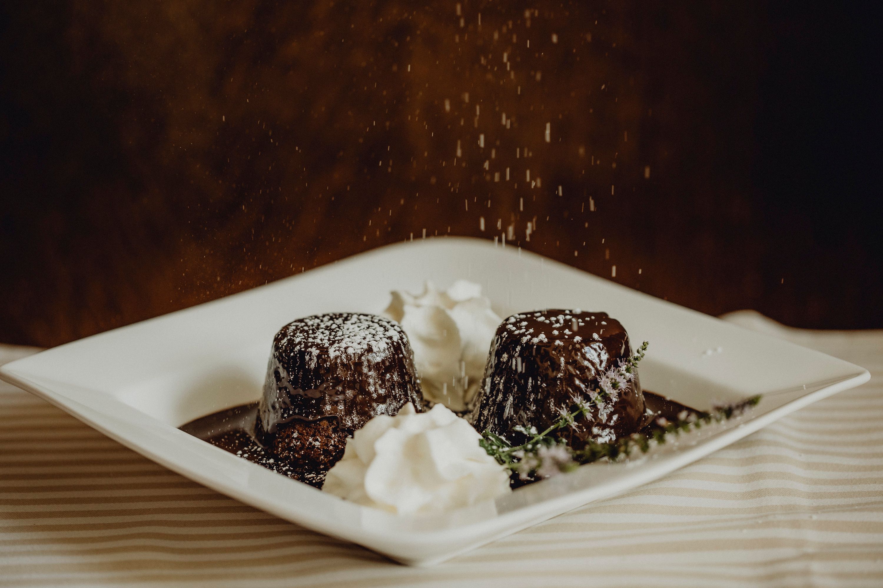 Two chocolate cakes with powdered sugar and cream on a plate.