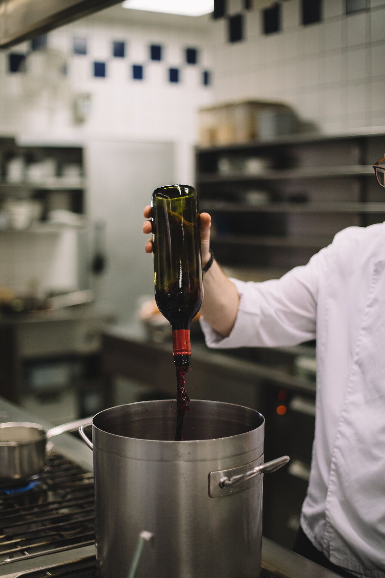 In der warmen Atmosphäre des Gasthauses wird ein edler Tropfen in einen großen Topf gegossen, während die Vorfreude auf ein köstliches Gericht steigt. Die Küche pulsiert vor Leben und der Duft von frischen Zutaten erfüllt den Raum, was die Gäste in eine genussvolle Stimmung versetzt.