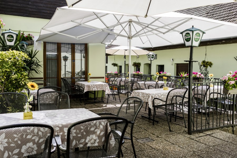 Gem&uuml;tliche Terrasse mit Tischen, St&uuml;hlen und Sonnenschirmen, dekoriert mit Blumen.