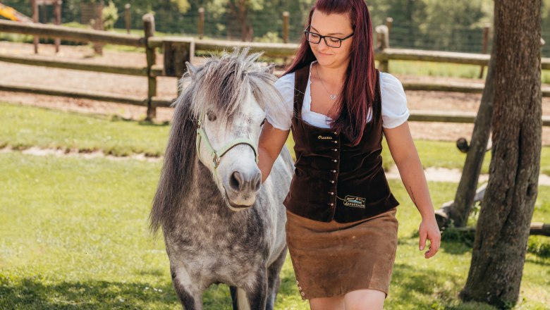 Claudia Langthaler führt ein Pony auf einer Wiese, im Hintergrund ein Holzzaun.