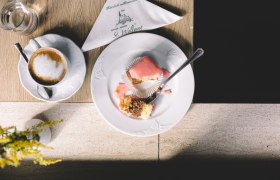 Ein Teller mit einem halben Punschkrapferl und eine Tasse Kaffee auf einem Tisch.