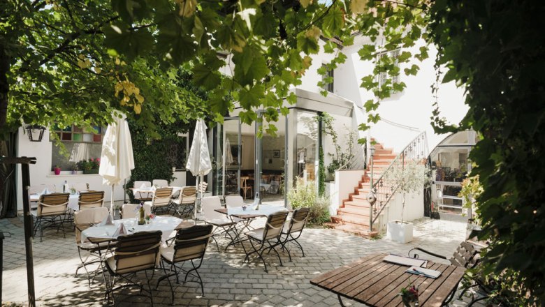 Gemütlicher Innenhof mit Tischen, Stühlen und grüner Laube.