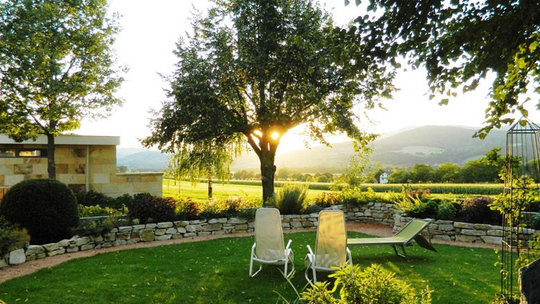 Ein Garten mit Liegestühlen, Bäumen und einer Steinmauer bei Sonnenuntergang.
