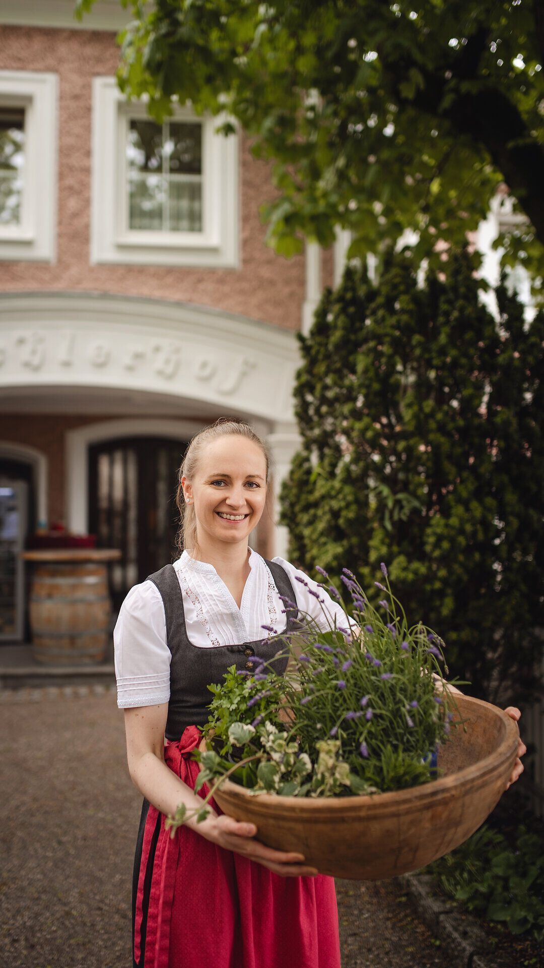 Inmitten der malerischen Landschaft des Mostviertels strahlt die Wirtin Maria Bachler mit einem Korb voller frischer Kräuter. Die sanften Hügel und die üppige Vegetation laden dazu ein, die Aromen der Region zu entdecken und die herzliche Gastfreundschaft zu genießen.