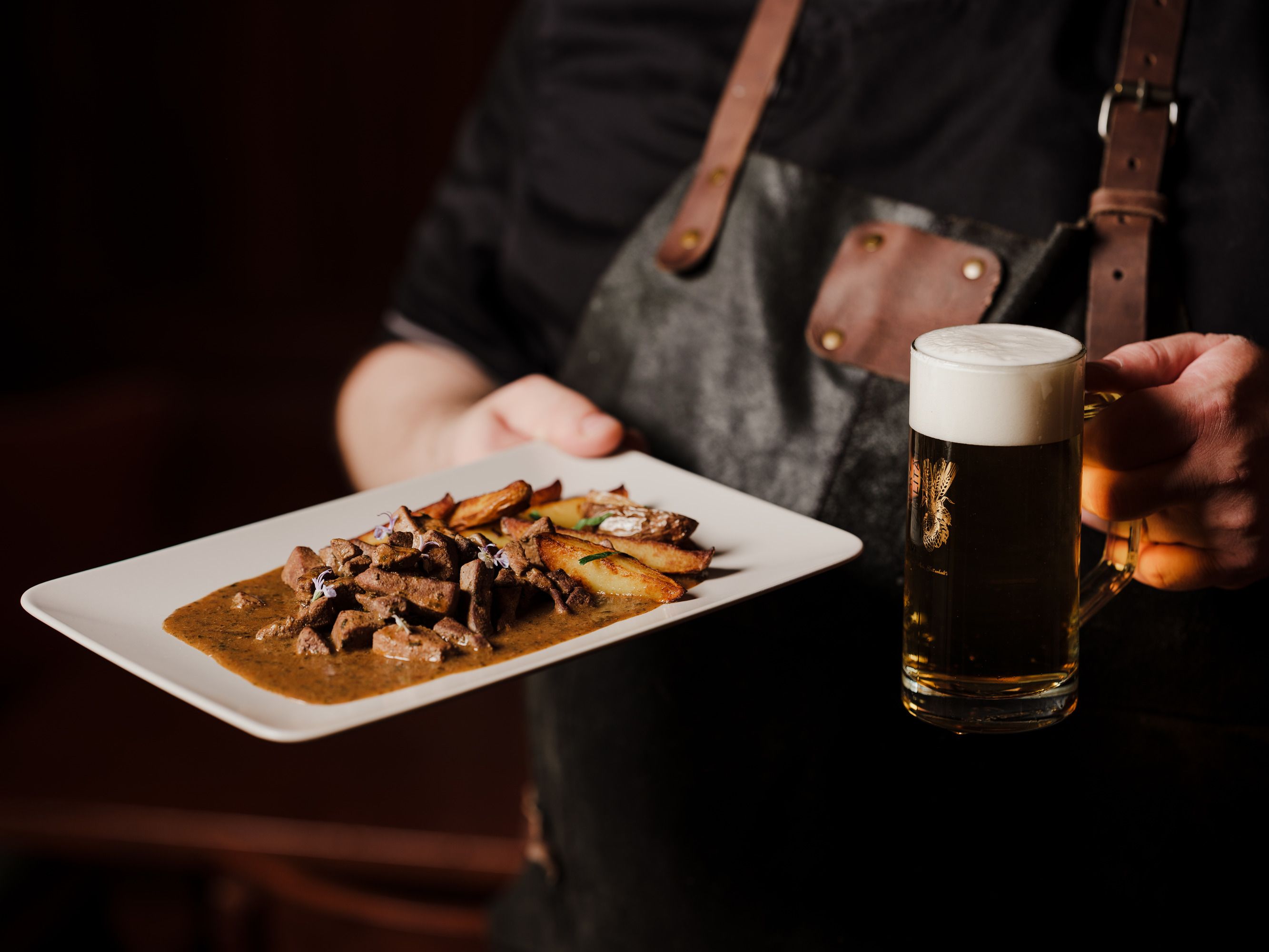 Person hält Teller mit Fleischgericht und Bierkrug in der Hand.