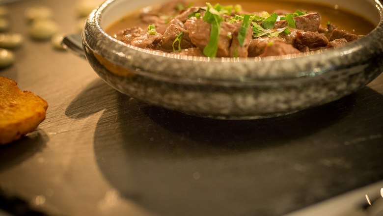 Ein Schokovulkan-Dessert auf einer Schieferplatte mit einer Kugel Eis und roten Rosenbl&auml;ttern dekoriert.