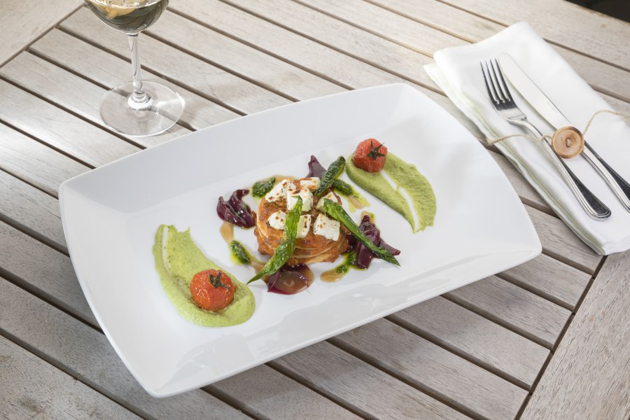 Gourmetgericht auf weißem Teller mit Gemüse und Soßen, daneben ein Glas Weißwein.