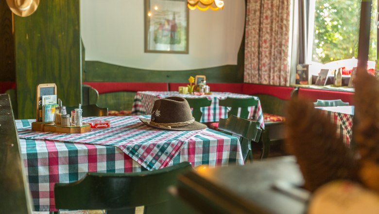Gem&uuml;tliche Gaststube mit karierten Tischdecken und einem Hut auf dem Tisch.
