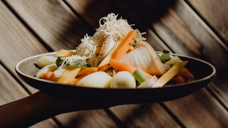 Ein Teller mit Krenfleisch, Gem&uuml;se und geriebenem Kren vor einer Holzwand.