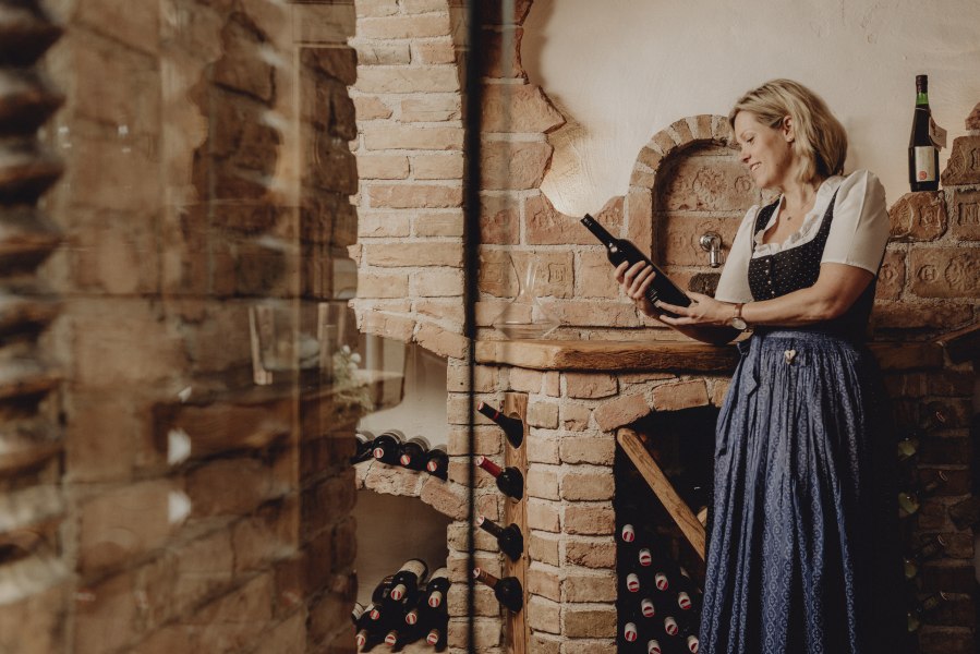 Frau in traditioneller Kleidung hält eine Weinflasche in einem rustikalen Weinkeller.