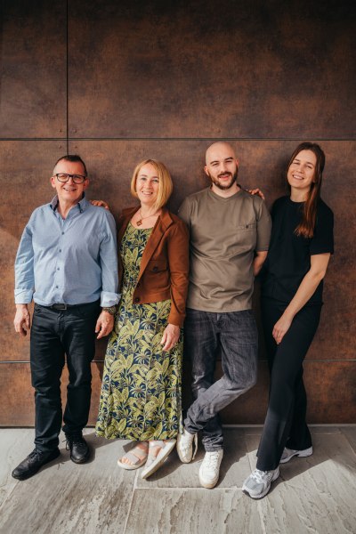 Vier Personen stehen l&auml;chelnd nebeneinander vor einer braunen Wand.