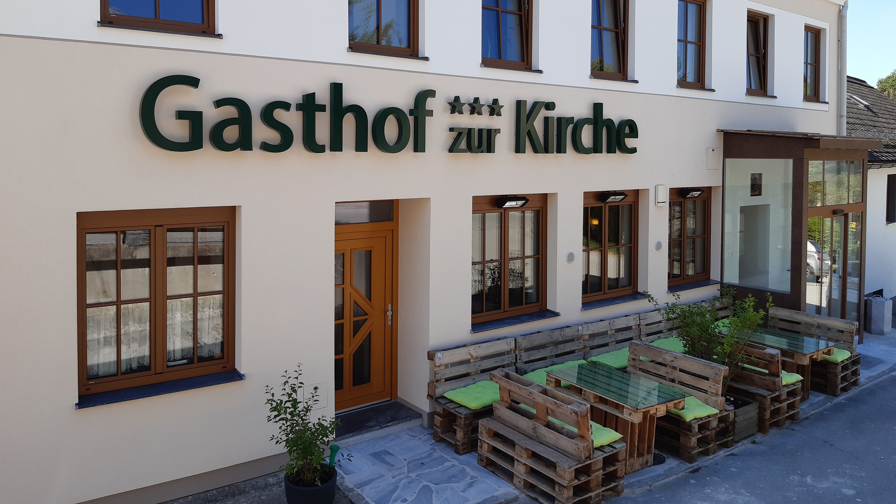 Fassade eines Gasthofs mit Holzpalettenmöbeln vor dem Eingang.