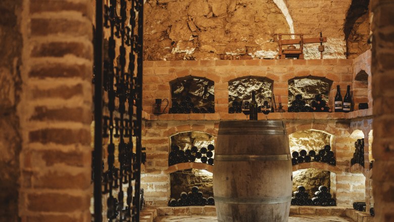 Ein rustikaler Weinkeller mit Ziegelw&auml;nden, Weinregalen und einem Holzfass in der Mitte.