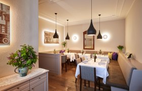 Elegantes Restaurant mit gedeckten Tischen, modernen Lampen und Blumenarrangement.