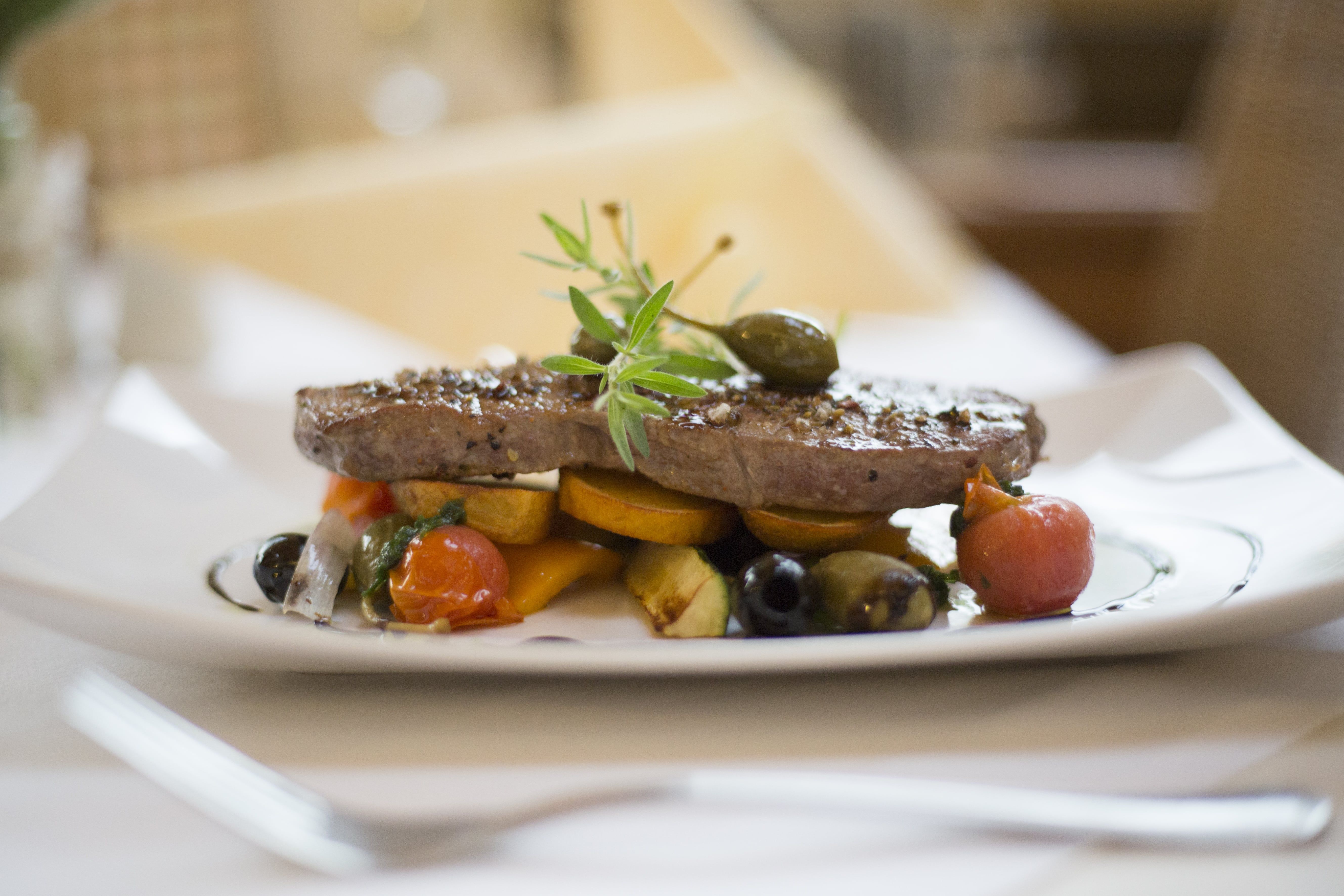 Ein Teller mit einem Stück Fleisch, garniert mit Gemüse und Kräutern.