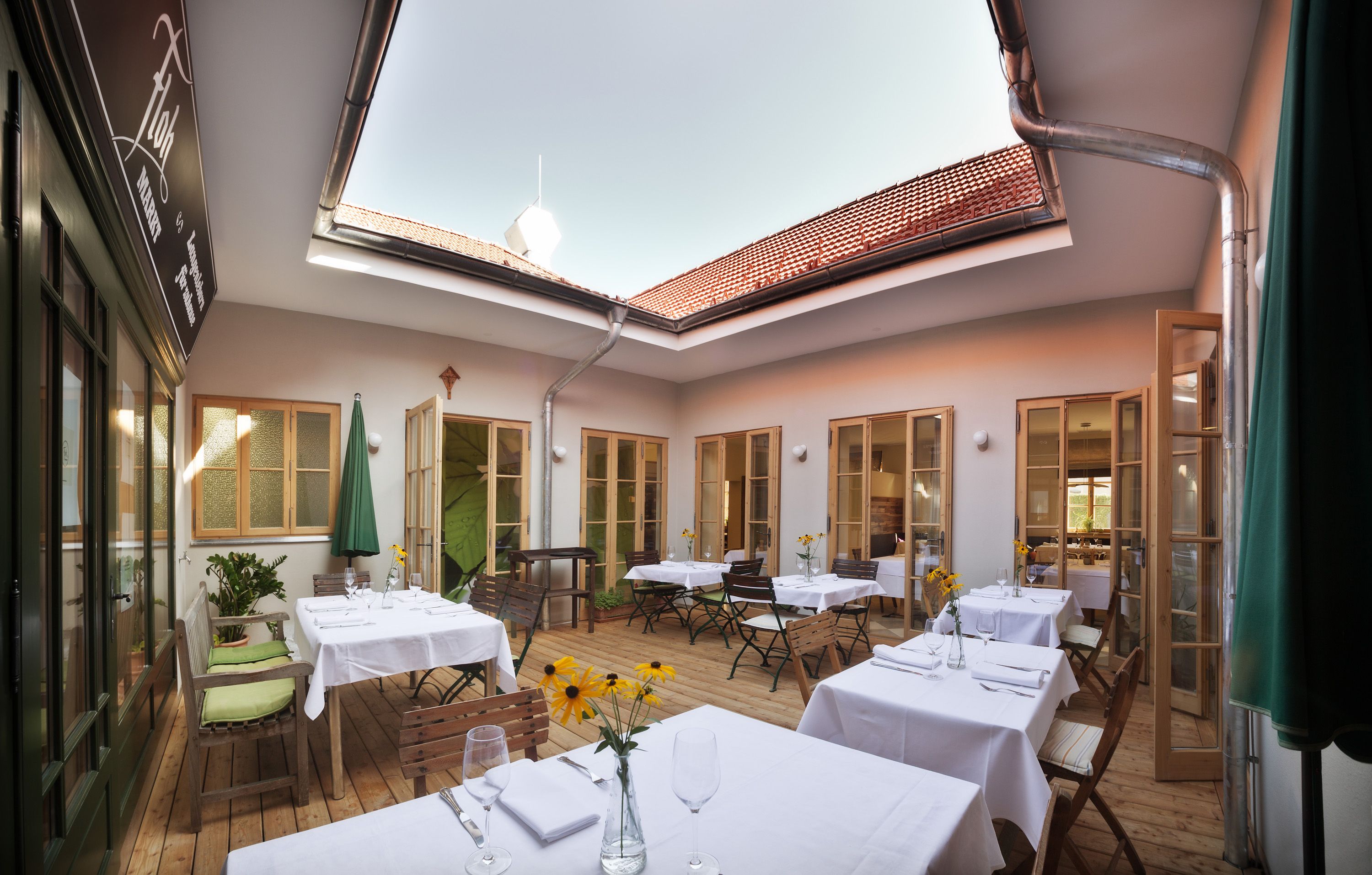 Innenhof eines Restaurants mit gedeckten Tischen und offenem Dach.