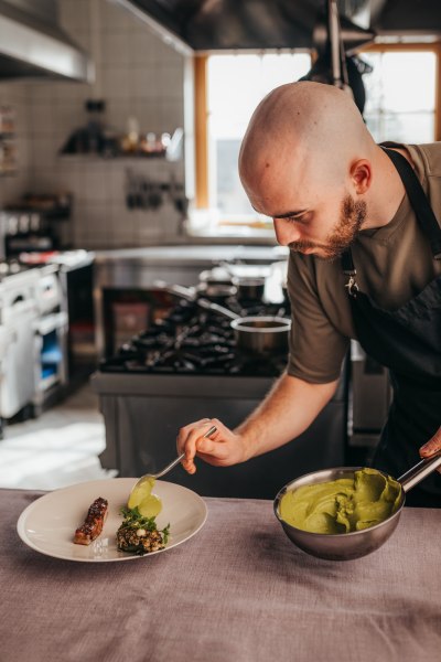Ein Koch richtet ein Gericht mit gr&uuml;nem P&uuml;ree auf einem Teller an.