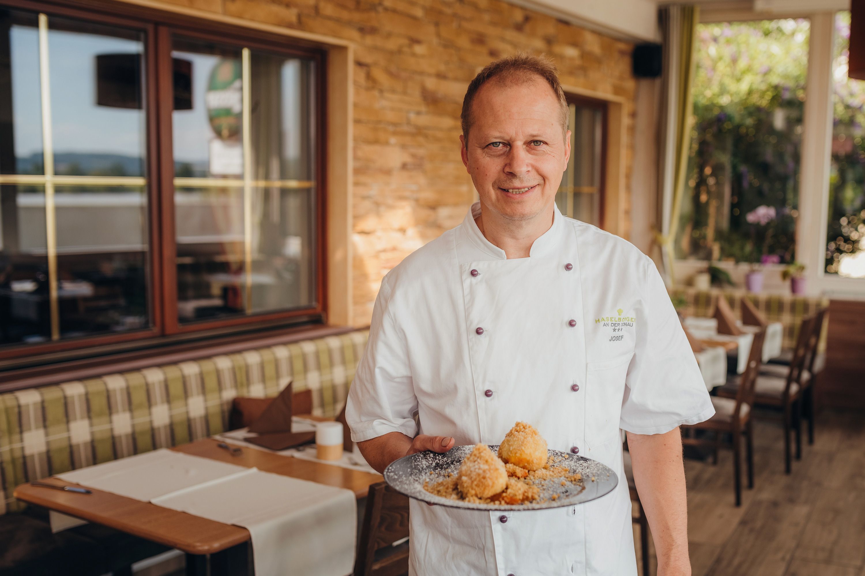 Koch in weißer Uniform präsentiert Teller mit Knödeln in einem Restaurant.