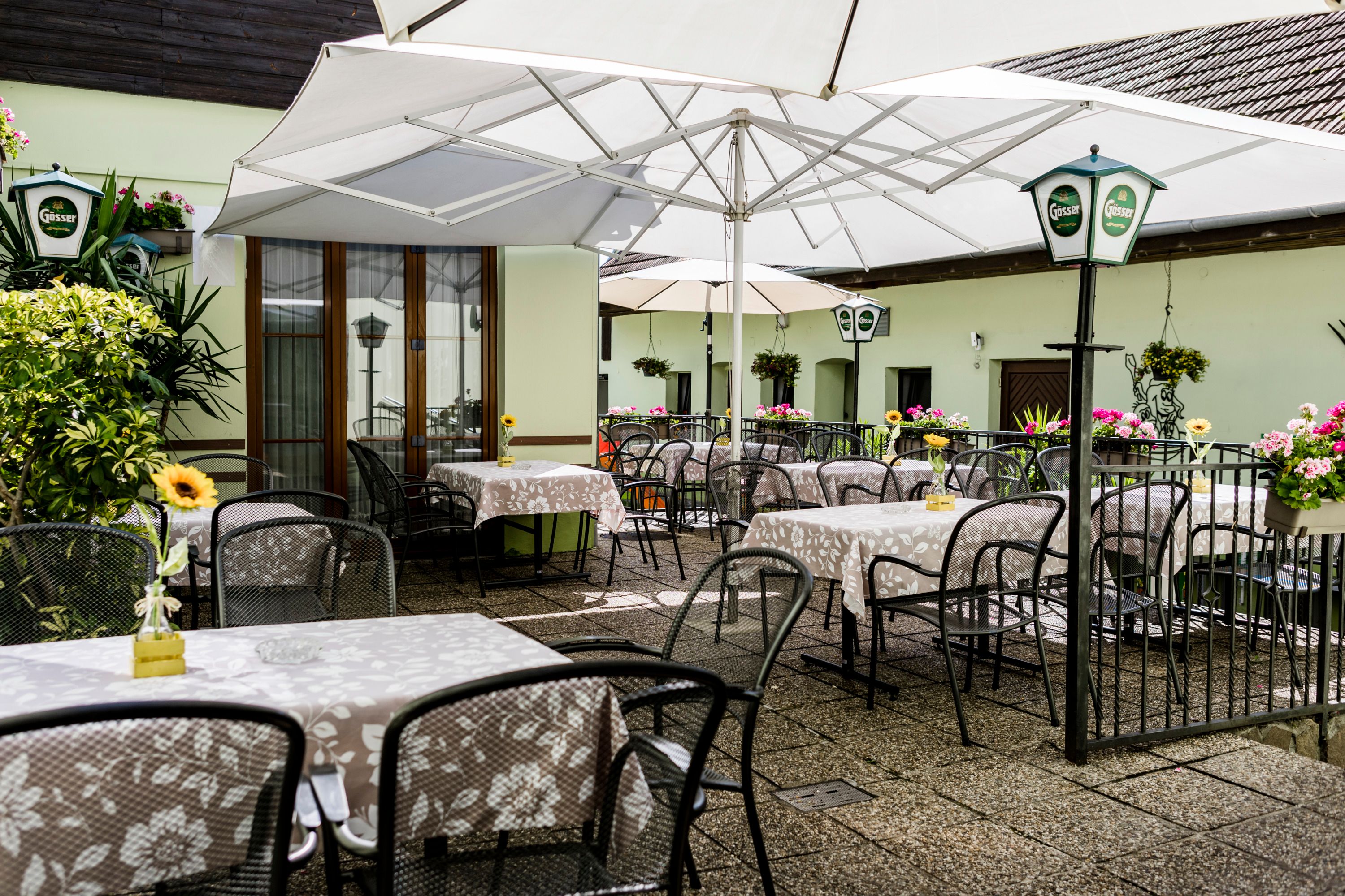 Gemütliche Terrasse mit Tischen, Stühlen und Sonnenschirmen, dekoriert mit Blumen.