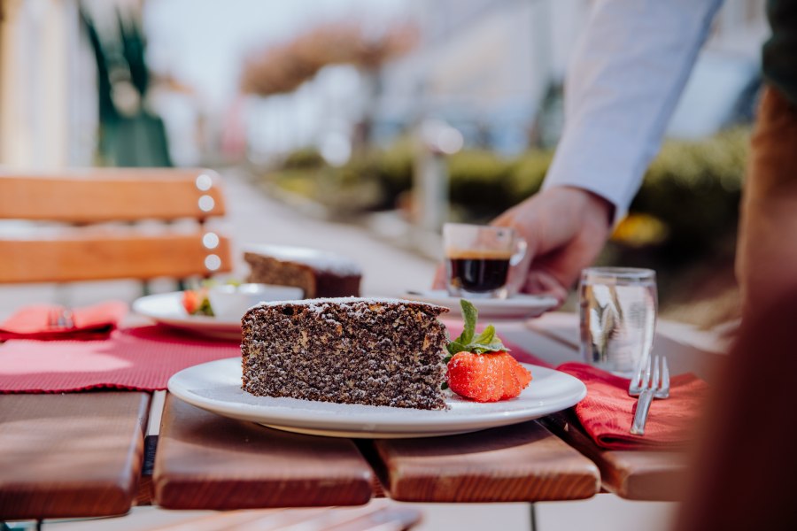 Mohnkuchen mit Erdbeere und Espresso auf einem Holztisch im Freien serviert.