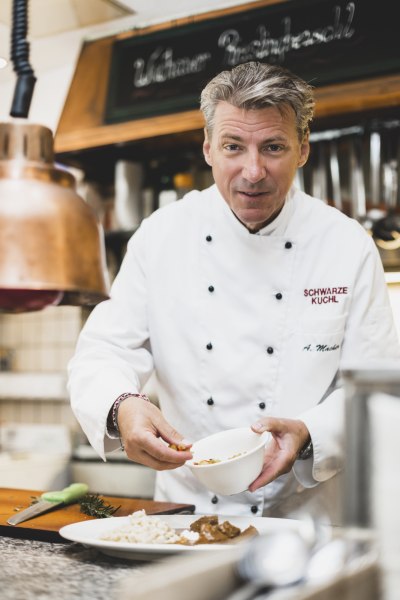 Koch in wei&szlig;er Uniform bereitet ein Gericht in einer K&uuml;che zu.
