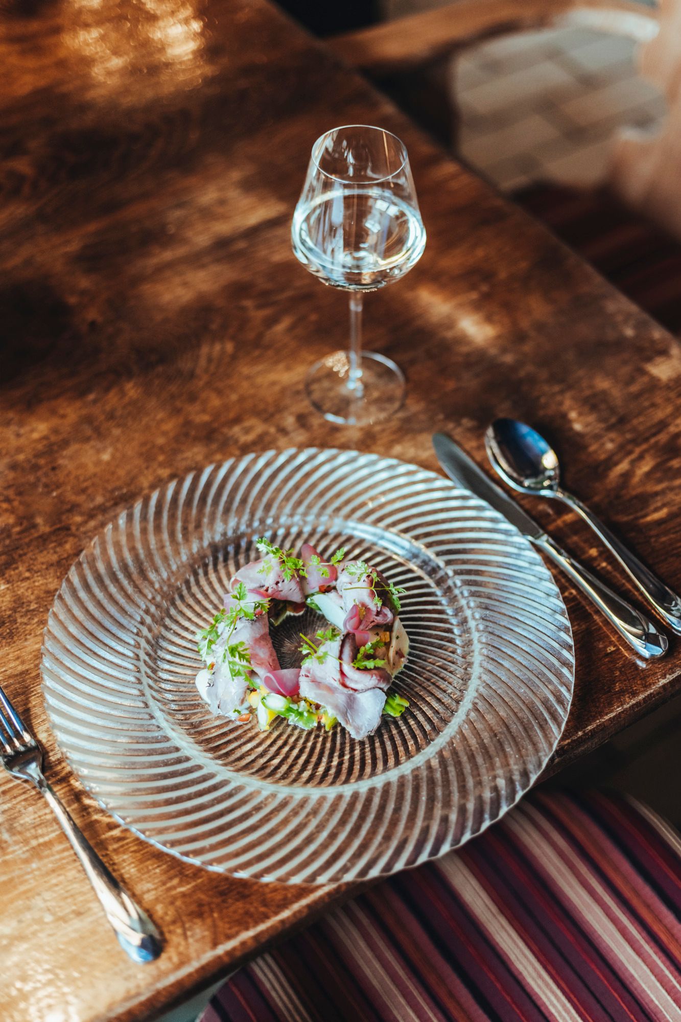 Ein Teller mit Roastbeef und Spargelsalat auf einem Holztisch, daneben ein Glas Weißwein.