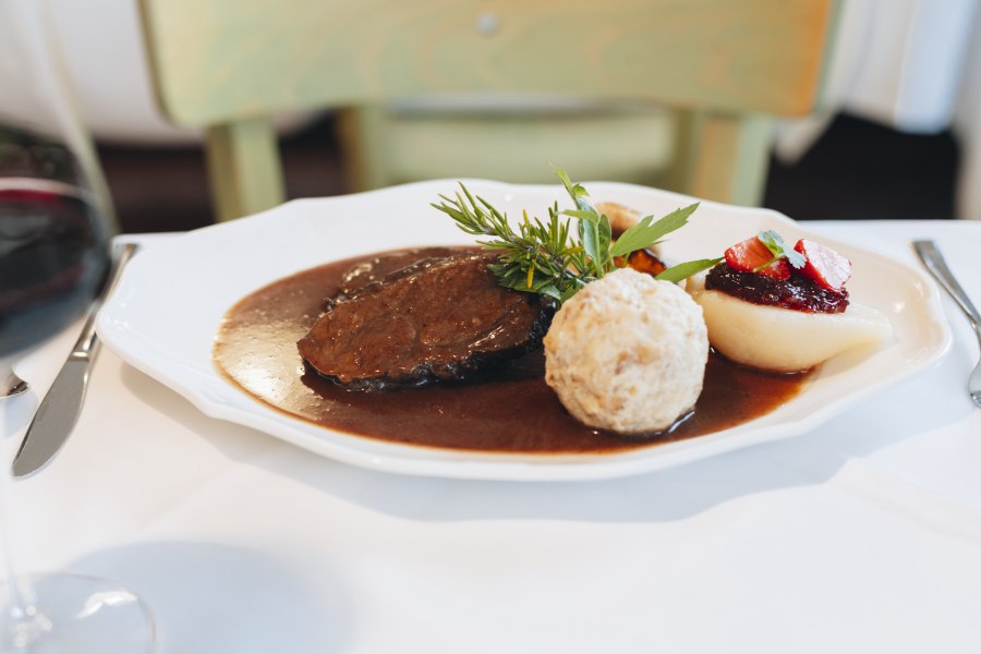 Ein Teller mit Hirschr&uuml;cken, Semmelkn&ouml;del, Birne mit Preiselbeeren und So&szlig;e, dekoriert mit Kr&auml;utern.