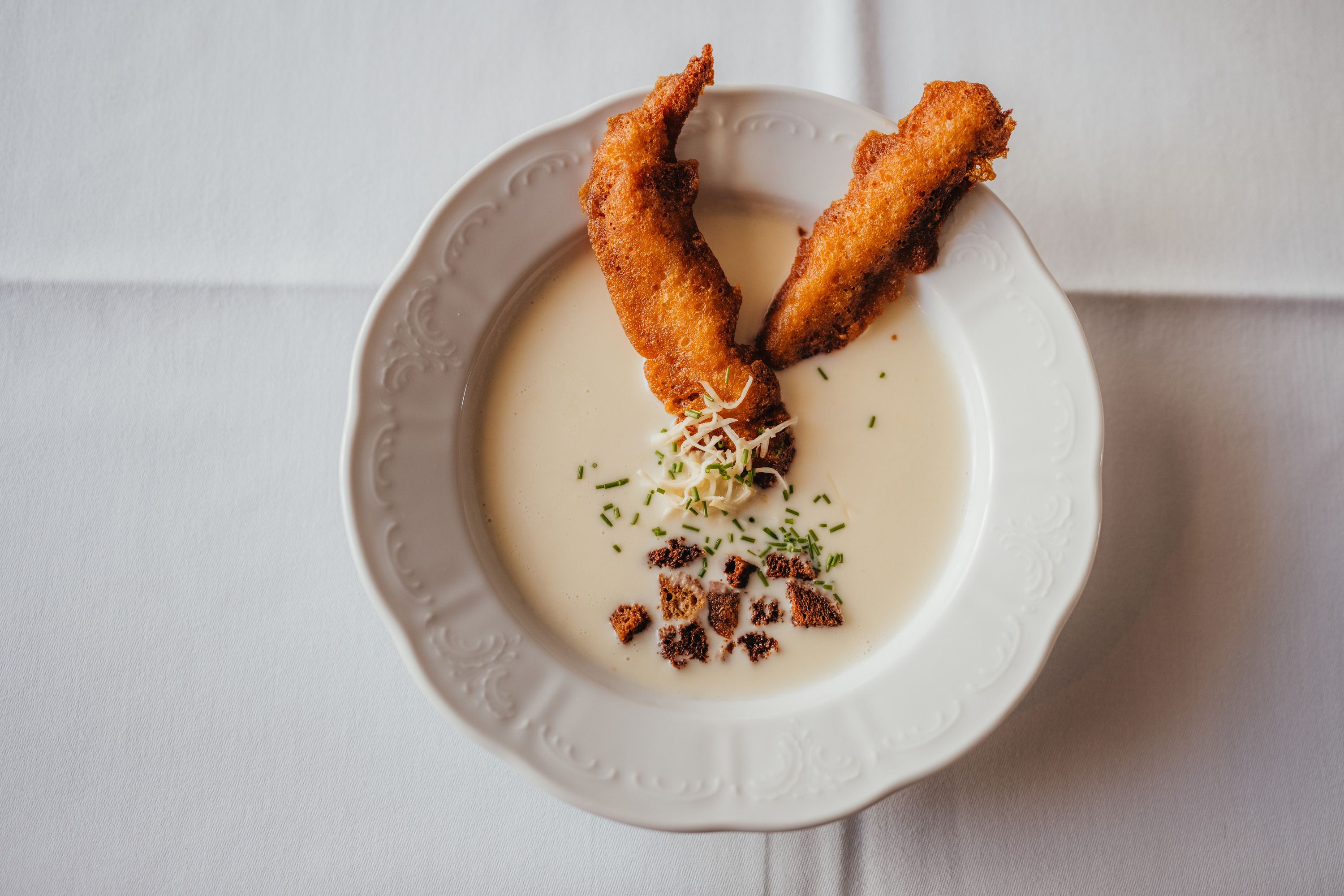 Cremige Suppe mit Räucherforellenstreifen und Kräutern auf weißem Teller.