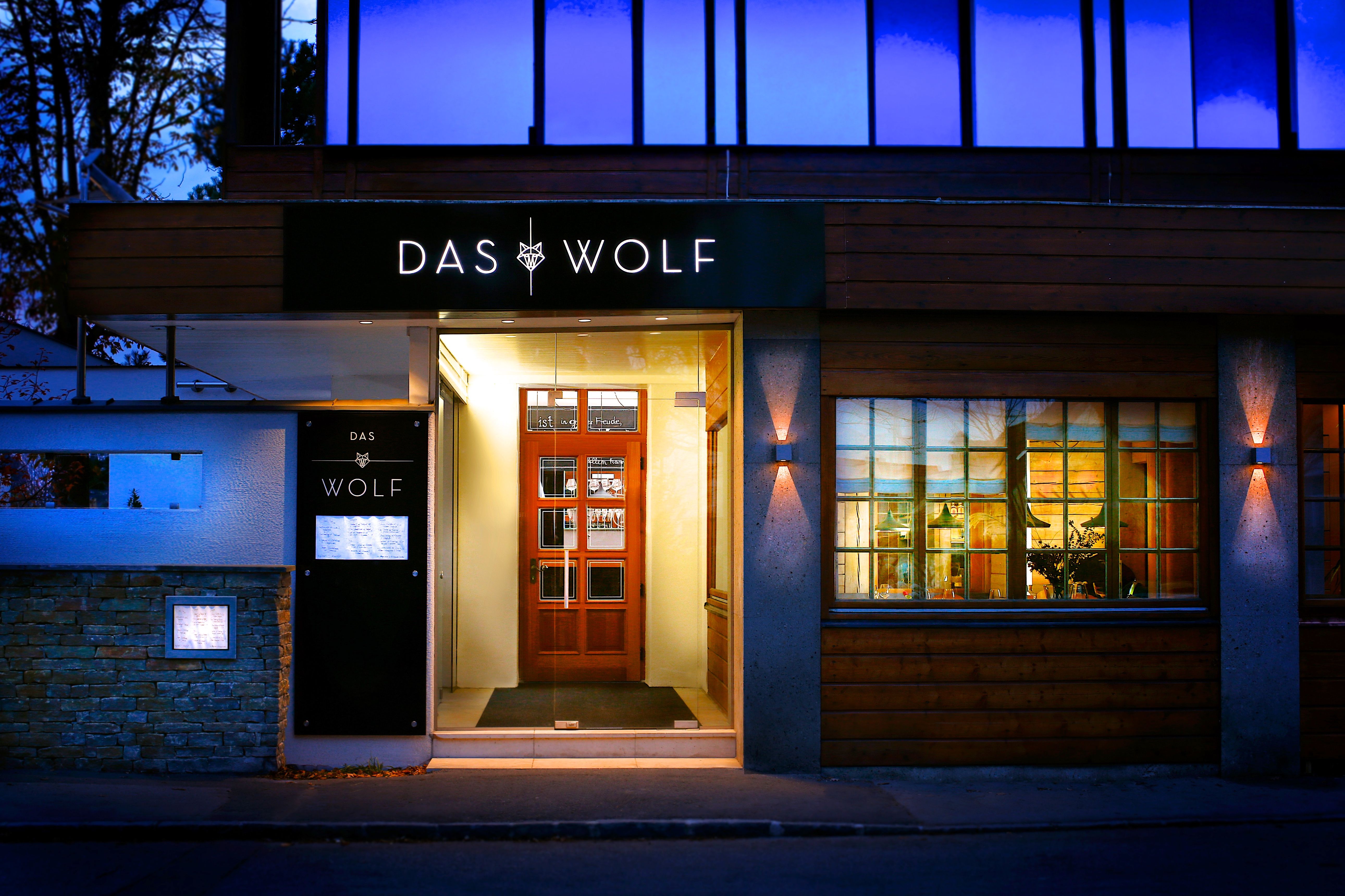 Restaurant Eingang in der Dämmerung mit hellem Lich an der Türe und Schriftzug das Wolf