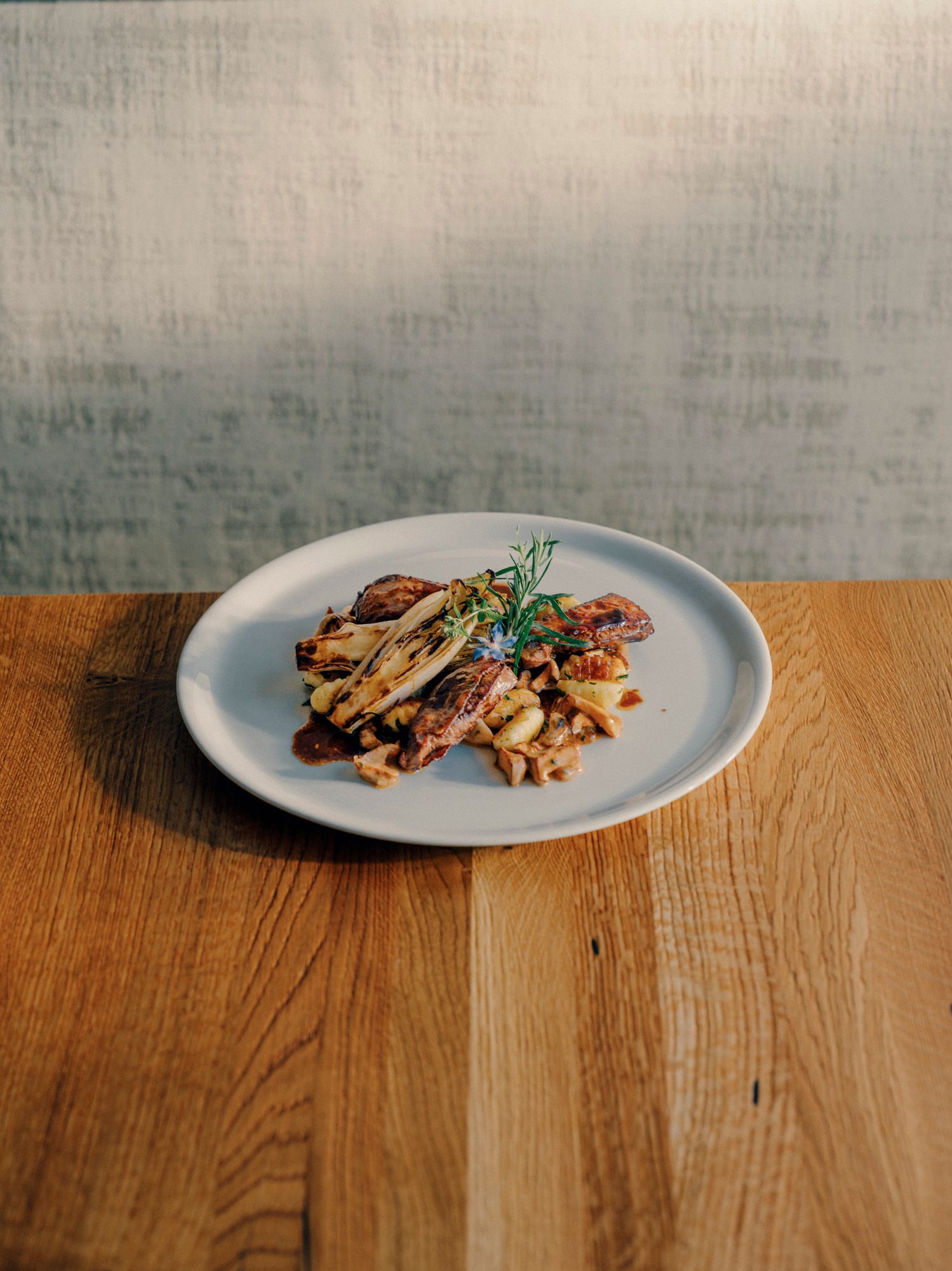 Ein Teller mit Saltimbocca vom Hirsch und Gnocchi auf einem Holztisch.