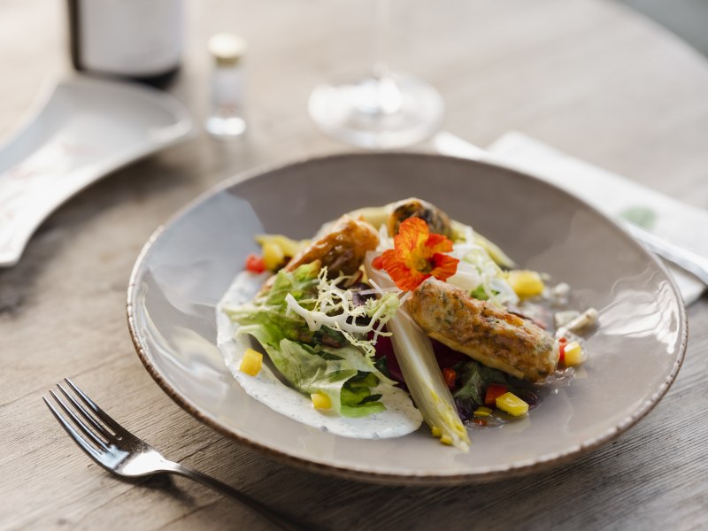 Ein Teller mit Fr&uuml;hlingsrollen, Salat und essbaren Bl&uuml;ten auf einem Holztisch.