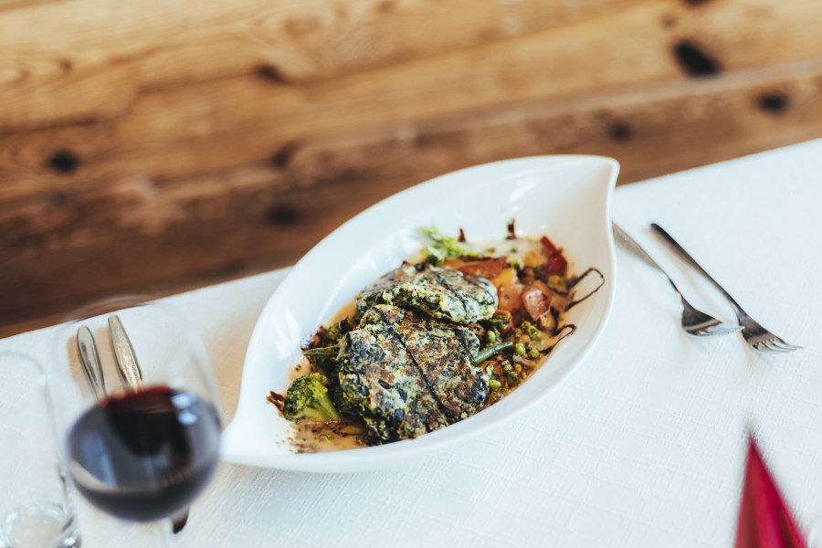Ein Teller mit Spinat Laibchen und Gem&uuml;se auf einem Tisch.
