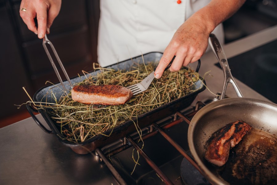 Ein Koch legt ein St&uuml;ck Hirschr&uuml;cken auf ein Bett aus Heu in einer Bratform.