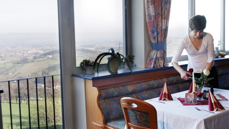 Eine Frau deckt einen Tisch in einem Restaurant mit Aussicht auf eine ländliche Landschaft.