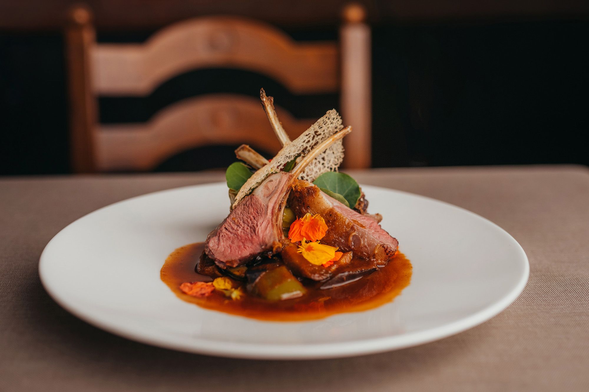 Gourmetgericht mit Lamm, Minipaprika, Brunnenkresse und Jus auf weißem Teller.