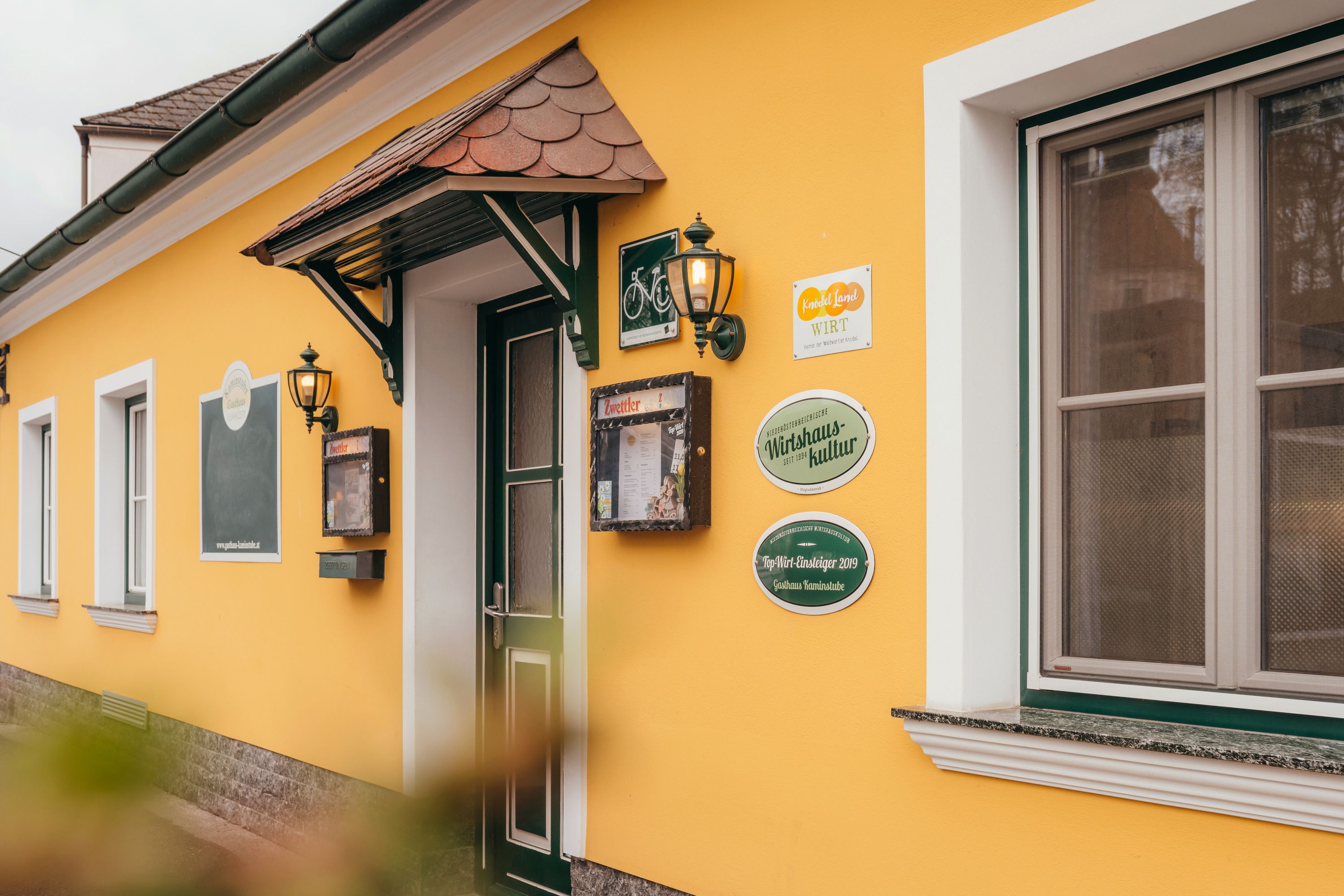 Gelbes Gebäude mit Tür und Fenstern, Schildern und Laternen an der Wand.