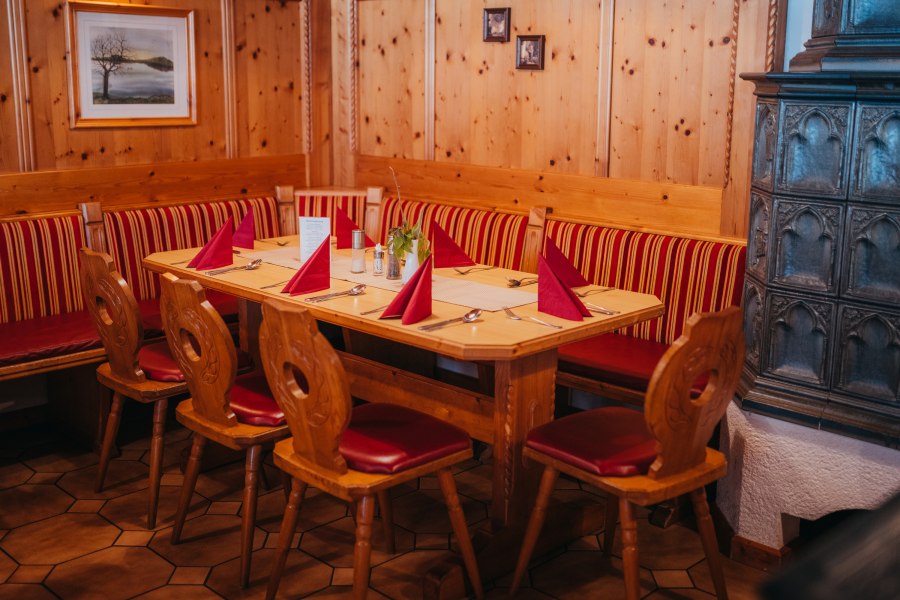 Gemütliche Stube mit Holzmöbeln, rotem Polster und Kachelofen.