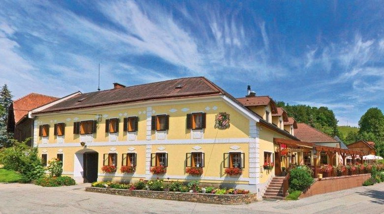 Traditionelles Gasthaus mit gelber Fassade, umgeben von grüner Landschaft und blauem Himmel.