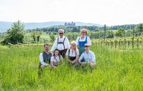 Eine Familie in traditioneller Kleidung posiert auf einer Wiese mit einem Schloss im Hintergrund.