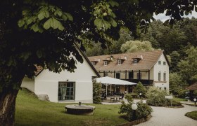 Ein idyllisches Wirtshaus mit Terrasse und Garten, umgeben von B&auml;umen.