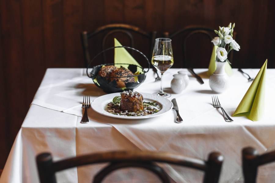 Ein gedeckter Tisch mit Tafelspitzsulz, Brot, einem Glas Weißwein und Blumen.