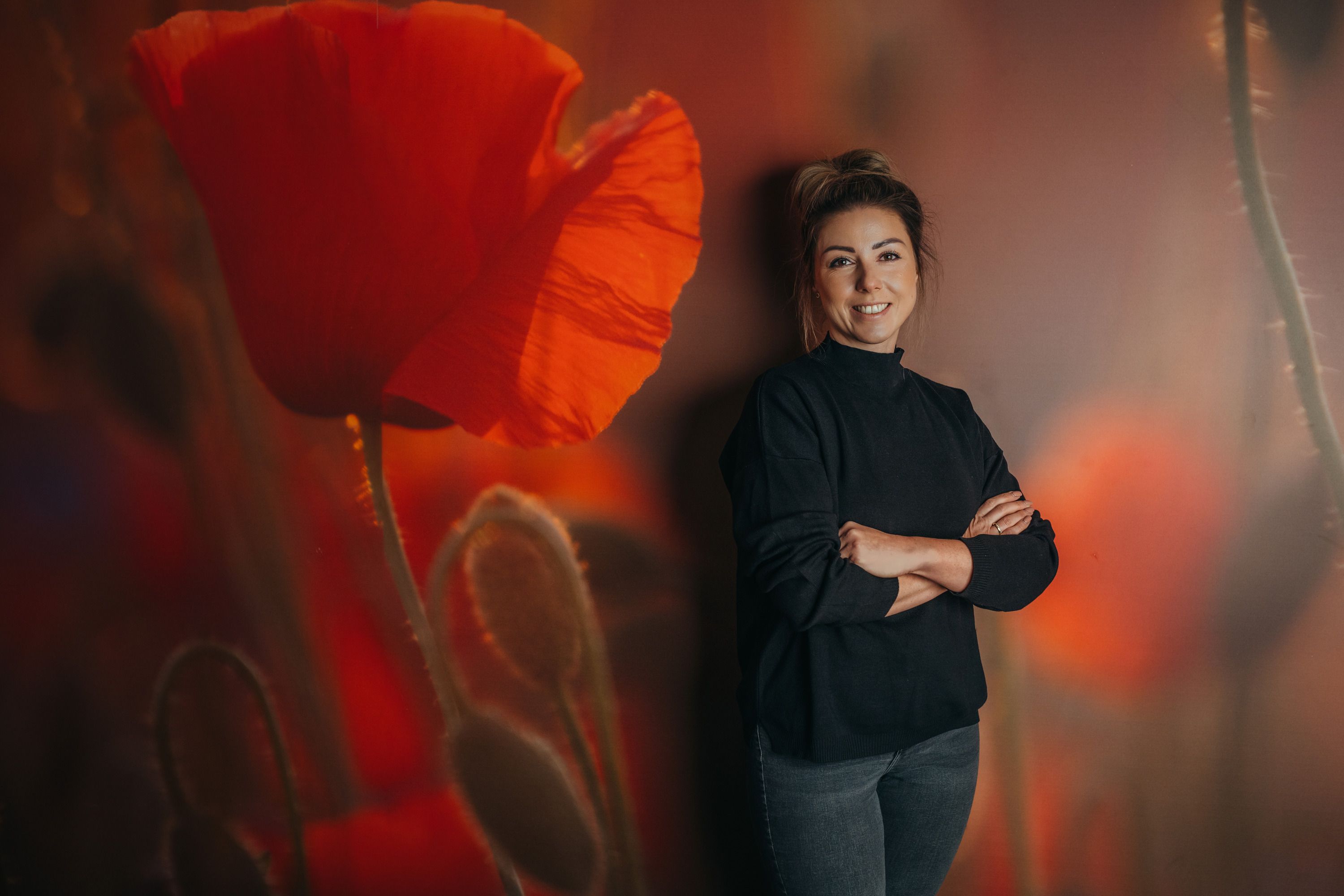 Frau steht vor einer Wand mit Mohnblumenmotiv.
