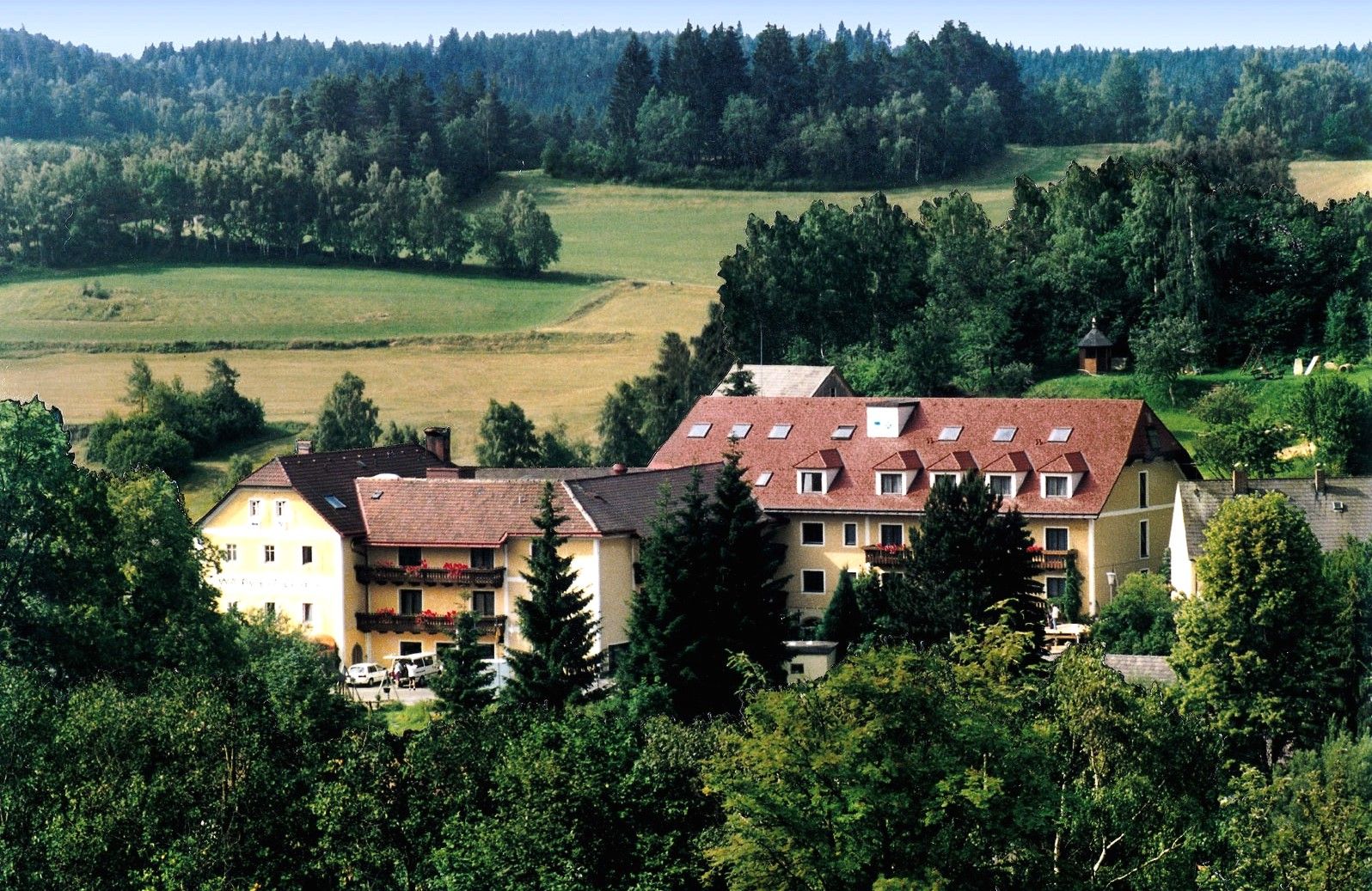 Ein großes Gebäude mit roten Dächern in einer grünen, bewaldeten Landschaft.