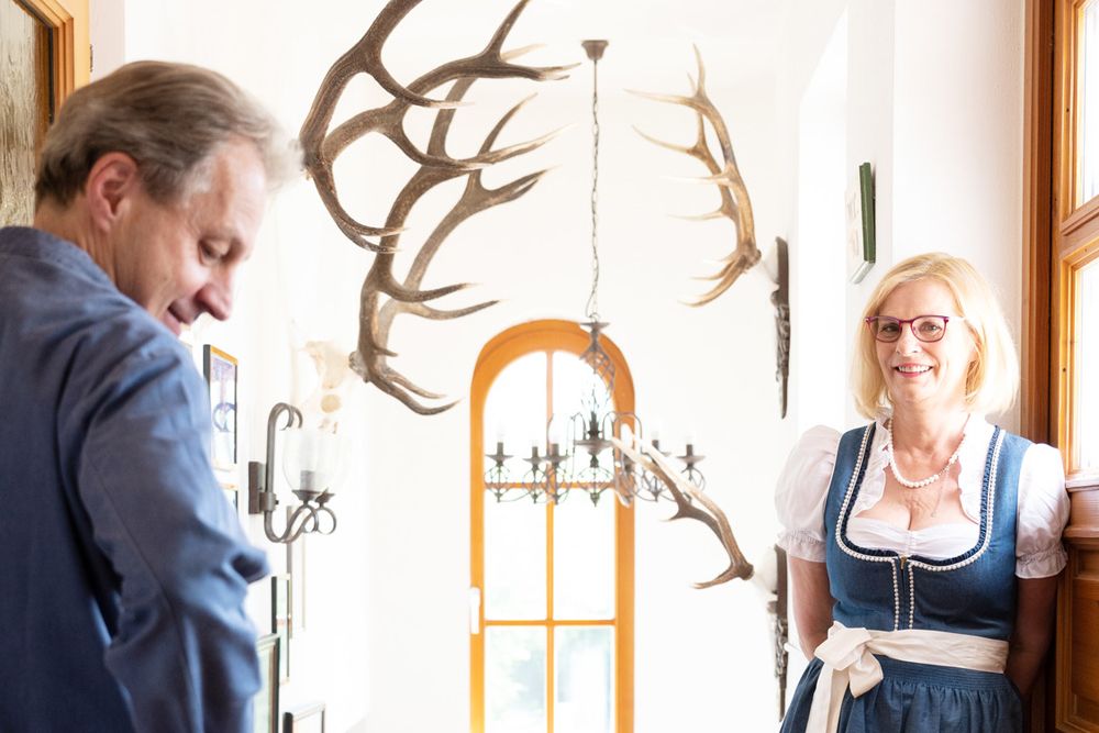 Ein Mann und eine Frau in traditioneller Kleidung stehen in einem Flur mit Geweihen an der Wand.